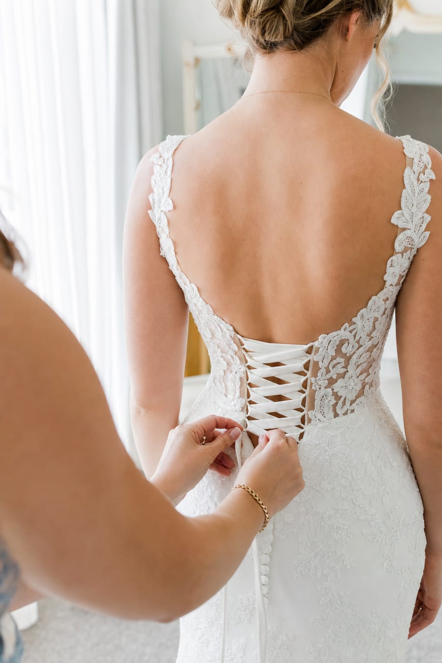 A bridal assistant lacing the corset back of a bride's lace wedding gown