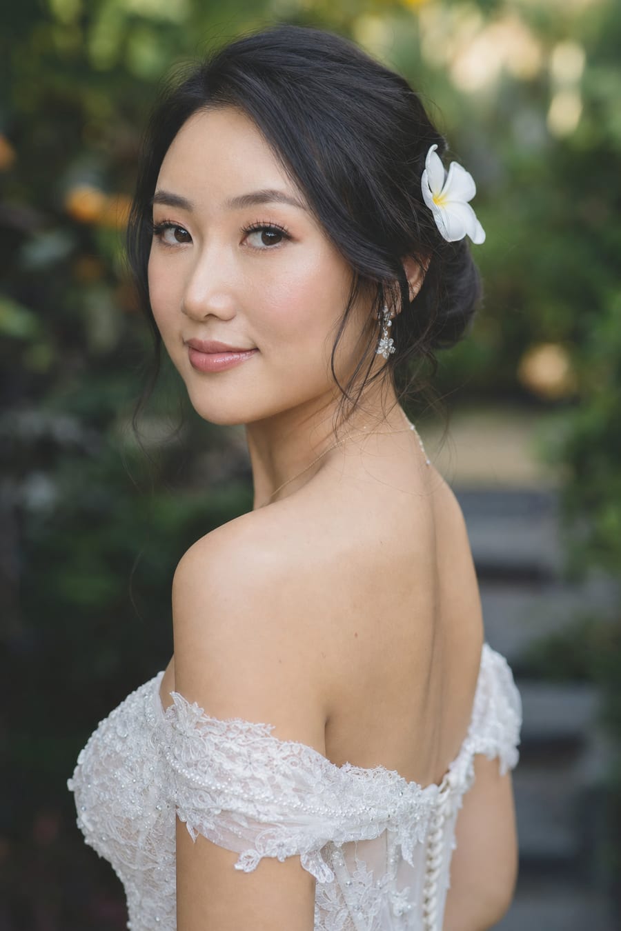 Close-up of an East Asian bride with soft glam wedding makeup and a low updo, a frangipani in her hair